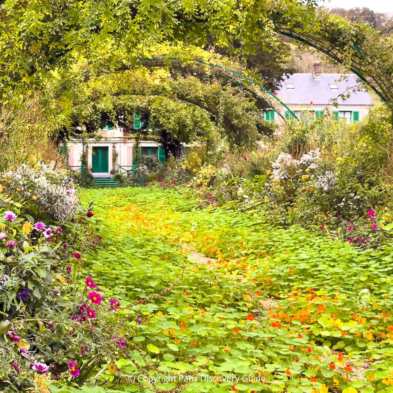 Late-blooming nasturtiums carpet the ground between masses of peonies and other flowers at Monet's pink and green Normandy farm house in Giverny