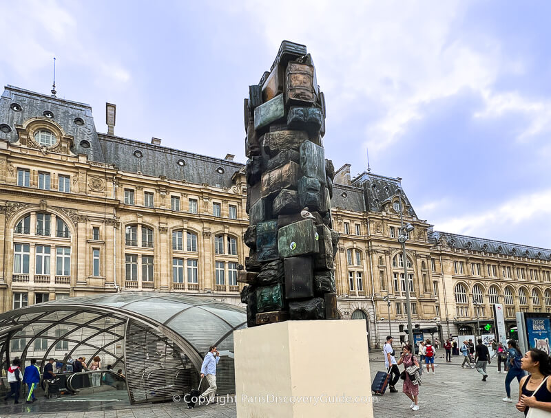 Metro station entrance and suitcase sculpture in Cour de Rome plaza in front of Gare Saint-Lazare