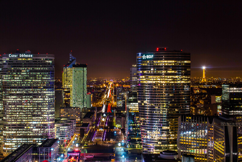 View from Grande Arche at night showing La Defense skyline and Paris skyline, including Arc de Triomphe and Eiffel Tower - Photo credit:  subterranologie.com, CC A-SA4.0 