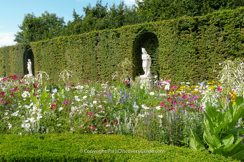 Statues in the walls of a Grove overlooking summer flowers at Versailles Gardens