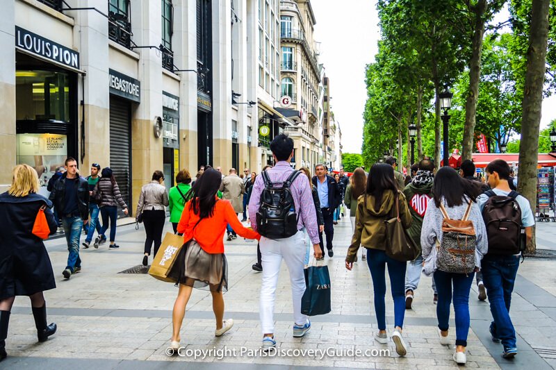 Shoppers strolling along Avenue des Champs Elysées' broad sidewalk lined by horse chestnut trees