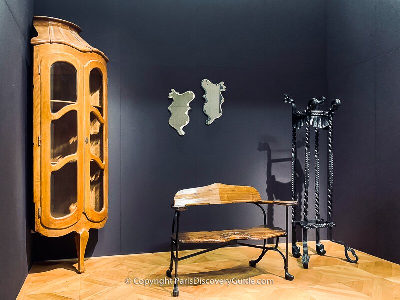 Corner display cabinet, church bench, mirrors. and wrought iron garden pot holder designed by Spanish architect Antoni Gaudí