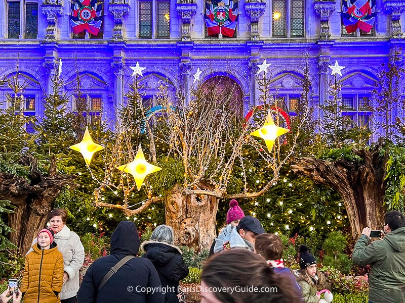 Another deer with lighted antlers peering out from the Christmas tree forest